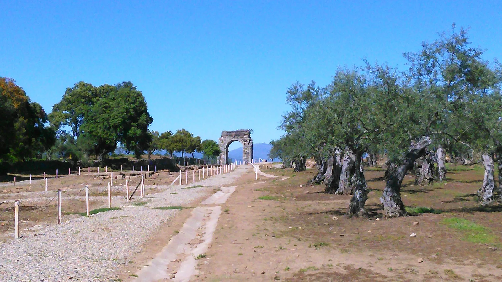 Tramo de la Vía de la Plata que entra en la ciudad romana de Cáparra, con el arco cuadrifronte al fondo